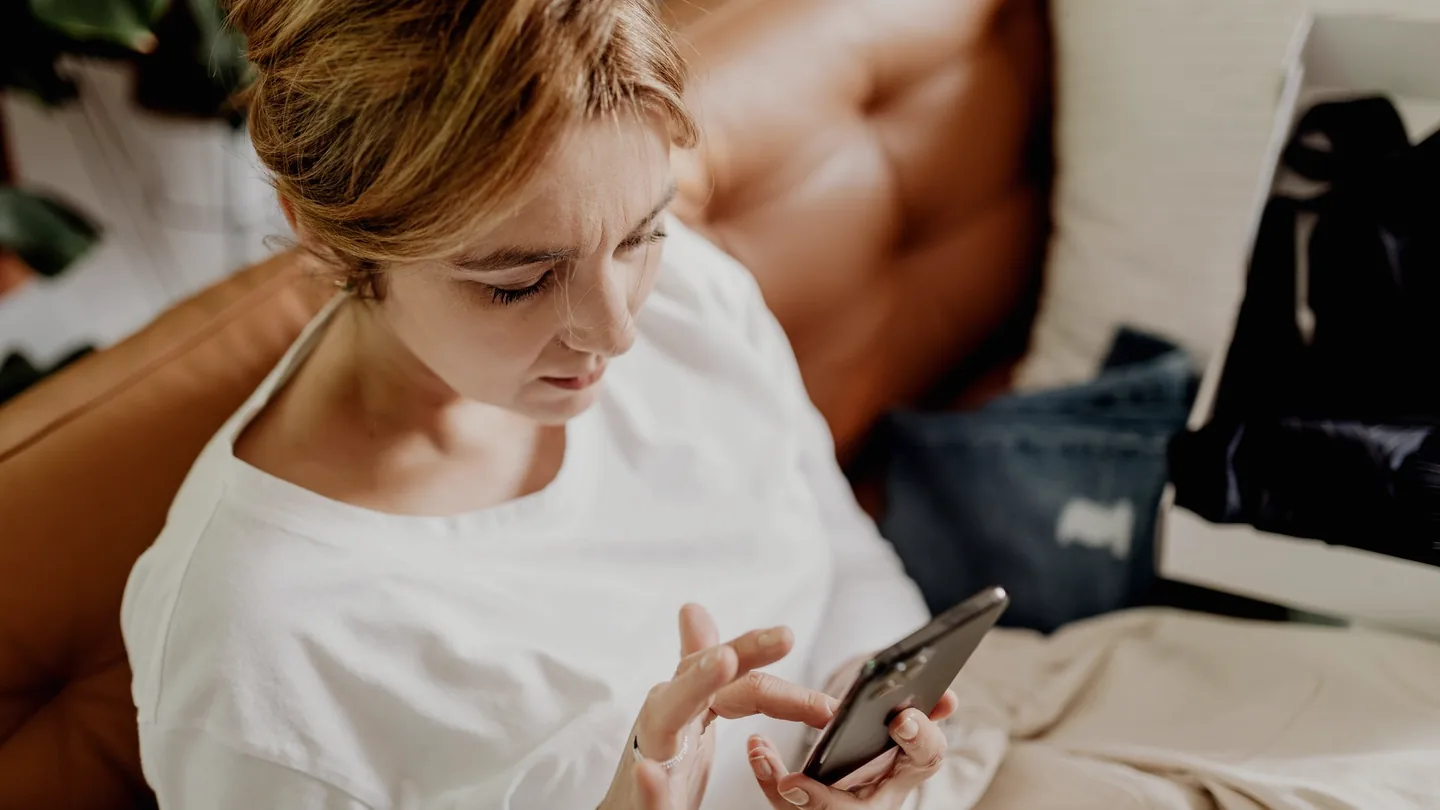Eine Person sitzt auf einem Sofa in einem dunklen Raum und scrollt durch eine App auf dem Smartphone