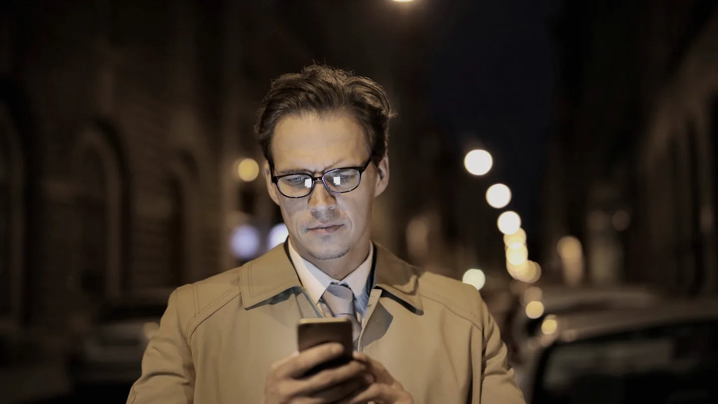 Um homem lendo uma mensagem no celular numa rua da cidade à noite