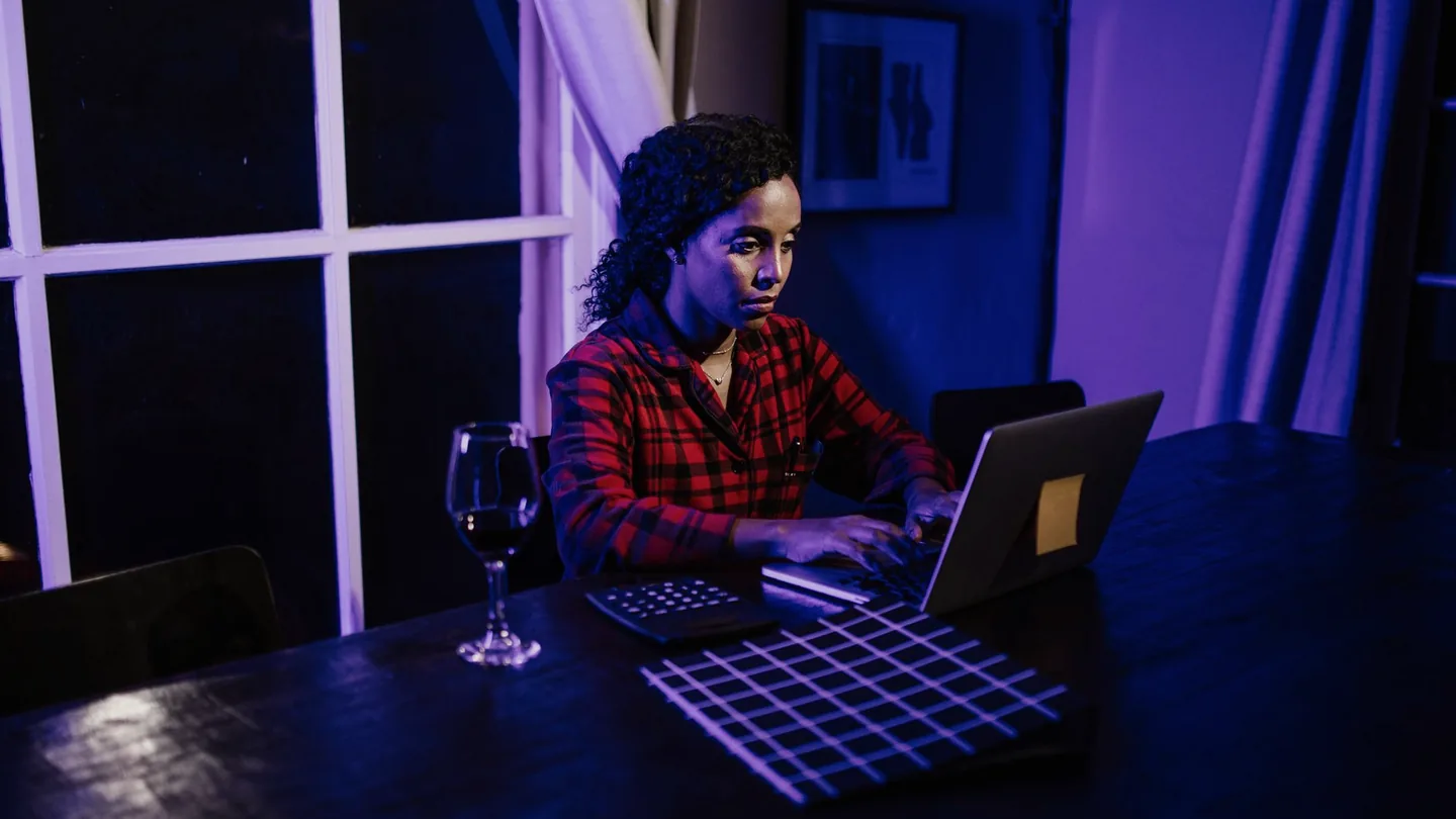 Una persona escribiendo en un portátil en la mesa de la cocina de madrugada, con la habitación iluminada solo por la pantalla